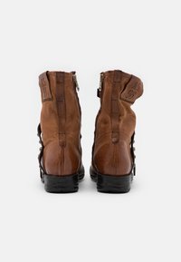 Stivali alla caviglia in pelle marrone con una texture opaca e lucida, cerniere posteriori e lacci decorativi sui lati. Logo impresso sul retro.