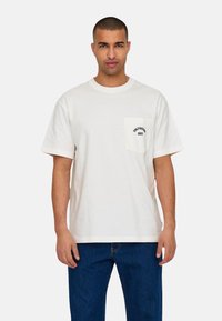 Witte katoenen t-shirt met korte mouwen, voorzien van een borstzak en zwarte tekst "ONLY & SONS 2013" op de zak.