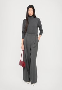 Un pull à col roulant gris charbon, un pantalon large à taille haute gris et un petit sac à main rouge ; un design élégant et ajusté. Des talons blancs.