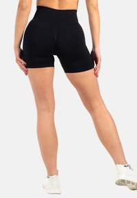 Shorts noirs taille haute en tissu extensible, avec une texture lisse et une coupe ajustée, mettant en valeur la taille et les jambes.