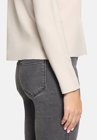 Beżowy sweter dzianinowy z długim rękawem w połączeniu z ciemnoszarymi dżinsami slim-fit. Sweter ma miękką fakturę i luźny krój.