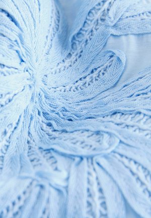 Hellblauer Strickstoff mit einem wirbelnden Muster, der strukturierte Rippen und filigrane spitzenartige Details aufweist und Weichheit sowie Flüssigkeit zeigt.