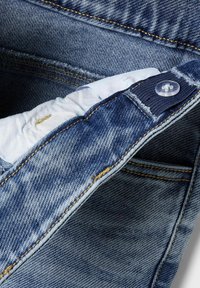 Jeans denim w ciemnoniebieskim kolorze, z delikatnym efektem wyblaknięcia. Pasek zawiera plastikowy guzik, a widoczne są detale szwów.