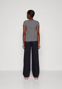 Camiseta gris a rayas y pantalones de mezclilla oscuros de pierna ancha, con cintura alta y dos bolsillos traseros. Llevados con zapatos de plataforma rosas.
