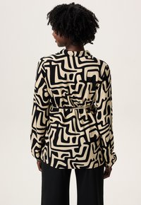 Langdurige mouwen shirt in beige stof met een zwart abstract patroon, met een strakke taille en knoopmanchetten.