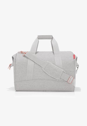 Sac de voyage en tissu gris avec deux poignées courtes, une bandoulière ajustable et des accents en rose gold. Texture lisse, forme rectangulaire.