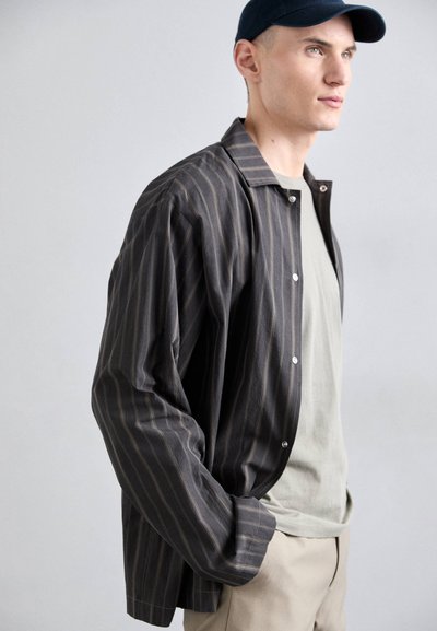 Cămașă cu dungi în gri închis cu dungi deschise, având o croială lejeră și mâneci lungi, purtată peste un tricou gri deschis.