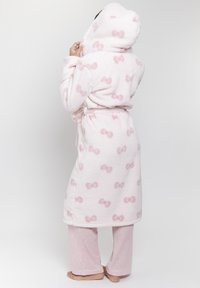 Mjuk rosa morgonrock med bågmönster, bälte i midjan och plyschtextur. Matchas med ljusrosa randiga byxor, barfota.