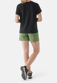 T-shirt nera a maniche corte, pantaloni corti verdi e scarpe da ginnastica nere con suola e lacci grigi. La vista posteriore mette in mostra una vestibilità comoda e un design semplice.