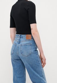 Černý body s krátkým rukávem v kombinaci se světle modrými džínami vysokého pasu, které mají koženou nášivku, zadní kapsy a volný střih.