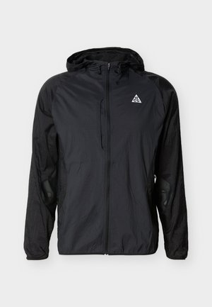 Melnā vieglā kapuces jaka ar pilnu priekšpuses rāvējslēdzēju, logotipu uz krūškurvja un elastīgiem aproces, paredzēta āra un ikdienas valkāšanai.