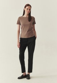 Haut marron à manches courtes avec encolure carrée, associé à un pantalon noir slim et des mocassins noirs. Texture lisse, coupe ajustée, accents minimalistes.