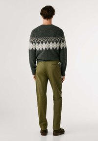 Knitovaná vlnená mikina v tmavosivej farbe s bielym a oranžovým geometrickým vzorom, skombinovaná s olivovozelenými nohavicami a hnedými topánkami. Zadný pohľad.