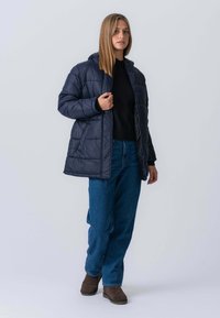 Marineblå quilted puffer-jakke med hætte, der har en frontlynlås, stikninger og en afslappet pasform, parret med blå denimjeans.