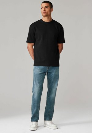Zwarte katoenen t-shirt met een ronde hals, gecombineerd met lichtblauwe denim jeans. Witte sneakers maken de casual outfit compleet.