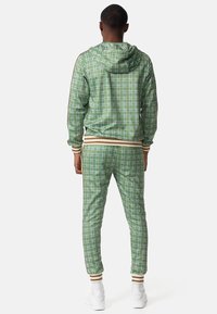Green plaid track jacket and matching pants, featuring a hood, ribbed cuffs, and white accents. Smooth texture with lightweight material.