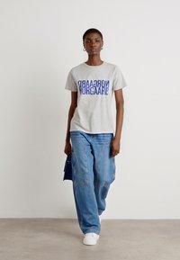 Gray cotton t-shirt with blue graphic text, paired with loose blue denim pants and white sneakers. Simple design in a neutral outfit.