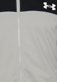 Gros plan d'une veste gris clair avec une fermeture éclair blanche et une partie supérieure noire avec un logo blanc Under Armour.