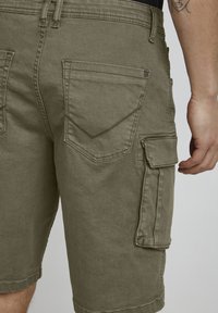 Cargo shorts in olijfgroen met een relaxte pasvorm, voorzien van meerdere zakken, stevig materiaal en een zichtbare naaddetail aan de achterkant.
