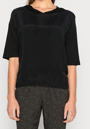 Zwart hoodie met een losse pasvorm, korte mouwen, een trekkoord bij de hals en een elastische zoom. Gecombineerd met zwart-gouden broek met patroon.