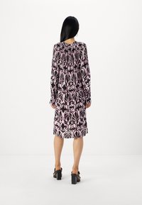 Langärmliges Kleid mit einem rosa-schwarzen Blumenmuster, gerafftem Rückendetail und knielangem Schnitt. Getragen mit sandalen mit Blockabsatz.