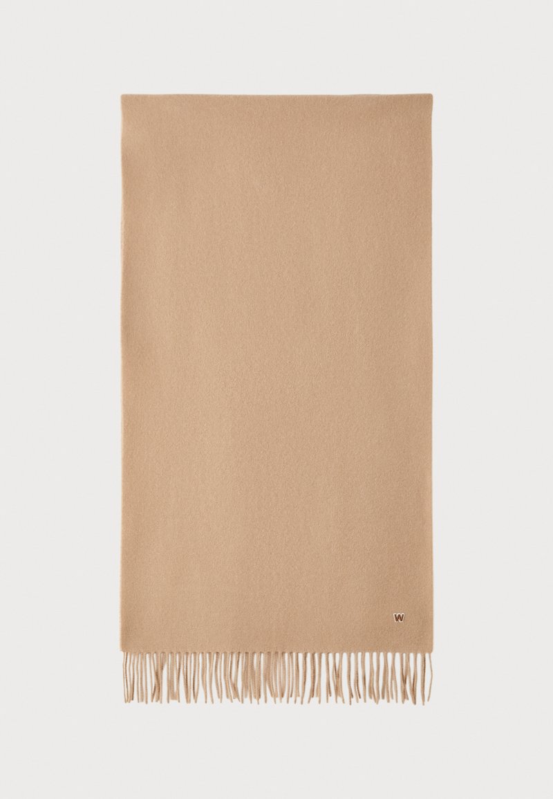 Écharpe en laine beige avec une texture douce, présentant des bords à franges et un petit logo dans un coin. Forme rectangulaire, finition lisse.