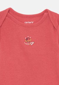 Red cotton onesie with a round neckline. Features a small embroidered design of a planet and rocket ship with stars. Brand label visible.