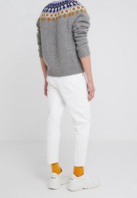 Grå stickad tröja med ett mönstrat ok i blått, gult och vitt, tillsammans med vita jeans och vita sneakers, med orangea strumpor.