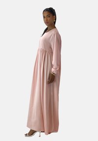 Robe longue rose en tissu doux, avec un col rond, des manches longues et une jupe fluide à coupe ample.