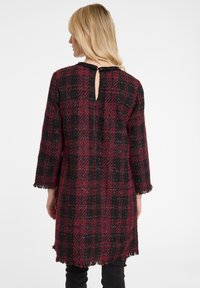 Kariertes Kleid in Dunkelrot und Schwarz, gefertigt aus strukturiertem Stoff mit Fransenbesatz an den Ärmeln und dem Saum, ausgestattet mit einer Schlüsselöffnung im Rücken.