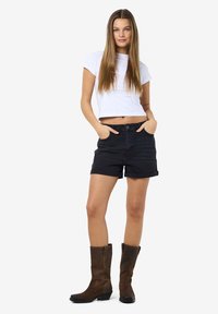 Black denim shorts with rolled cuffs, paired with a white cropped t-shirt. Brown knee-high boots with a low block heel. Standing pose.