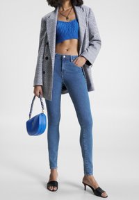 Džíny s vysokým pasem, texturovaný modrý pletený crop top, kostkovaný blejzr, černé sklouznuté podpatky a modrá kabelka s copánkovým popruhem.