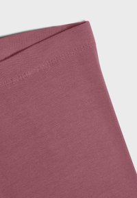 Gros plan sur un tissu en coton rose, présentant une texture lisse et un bord plié avec des coutures visibles, mettant en valeur ses détails de conception.