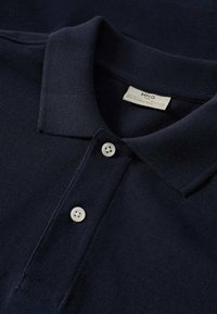 Polo shirt bleu marine en tissu tricoté texturé, avec un col, un rabat à trois boutons et une étiquette cousue à l'intérieur du col.