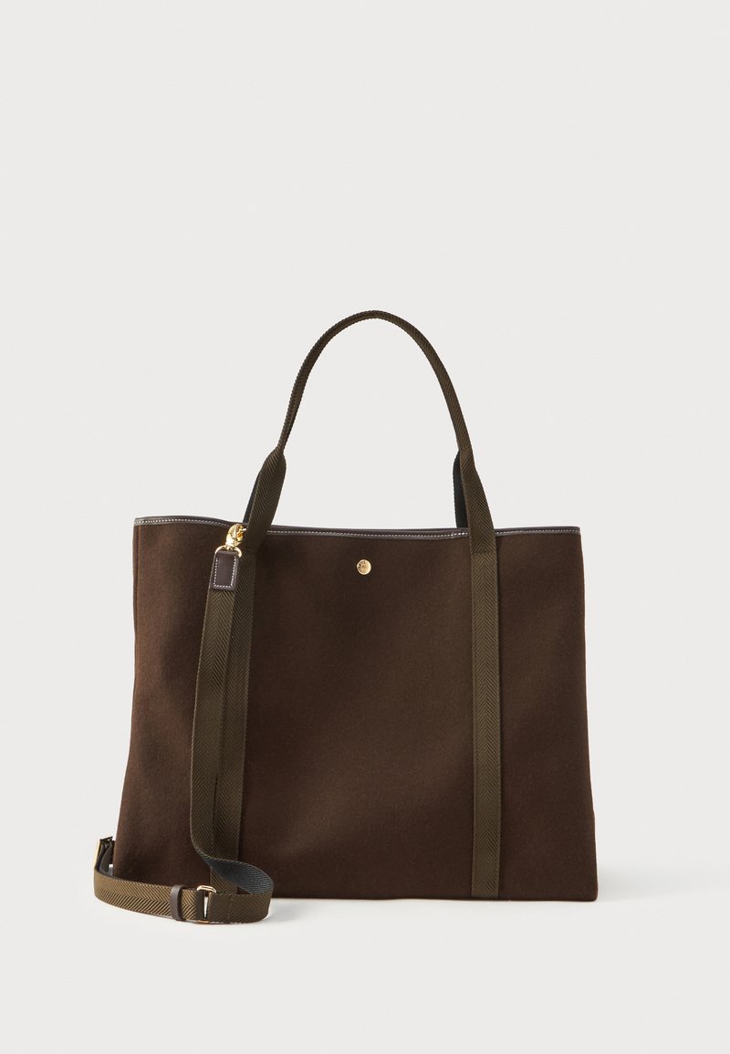 Καφέ υφασμάτινη τσάντα tote με σκούρες πράσινες λαβές και χρυσή λεπτομέρεια. Διαθέτει ορθογώνιο σχήμα και λεία υφή.