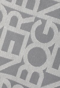 Un textile gris présentant un motif de grandes lettres et formes blanches. La texture est tissée, avec des éléments en relief et une finition lisse.