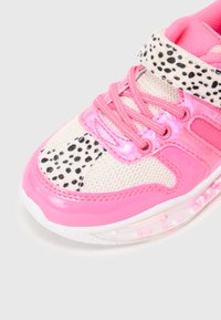 Zapatilla deportiva rosa con un cuerpo de malla, acentos rosas brillantes y una superposición impresa moteada. Incluye cordones y una correa de gancho y bucle.