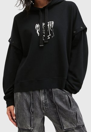 Sweat à capuche noir avec un graphique abstrait de visage blanc et du texte, porté avec un pantalon cargo noir délavé.