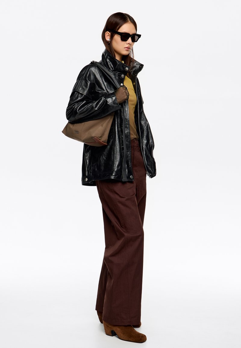 Chaqueta negra de imitación cuero, top verde oliva, pantalones anchos marrones, botines de ante marrones, gafas de sol negras, con bolso de hombro color beige.