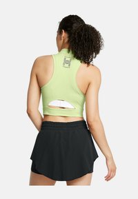 Svetlozelený športový crop top s dizajnom na preteky, ktorý má otvorený detail na chrbte a logo. V kombinácii s čiernymi skortami.