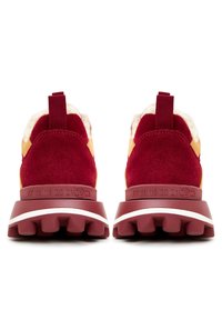 Sneaker in suede rossa e gialla con colletto imbottito, suola in gomma testurizzata e un tab di trazione sul retro. Presenta numeri in rilievo sul tallone.