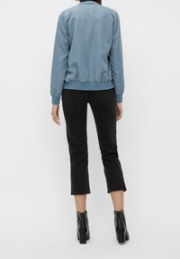 Lys blå bomberjakke med ribbede manchetter og kant, parret med sorte cropped jeans og sorte ankelstøvler. Glat tekstur, afslappet pasform.
