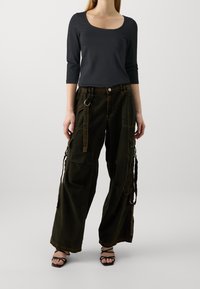 Black long-sleeve top paired with loose, dark green cargo pants featuring pockets, a belt, and adjustable straps on the sides.
