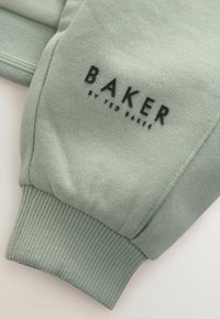 Jasnozielona bluza z ribbrowymi ściągaczami, z czarnym logo "BAKER by TED BAKER" na przodzie. Miękka tekstura, casualowy styl.
