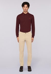 Bordowa koszula polo z długim rękawem i kołnierzykiem oraz kontrastowym wykończeniem, zestawiona z beżowymi spodniami typu slim fit i brązowymi butami. Prosty detal logo na koszuli.