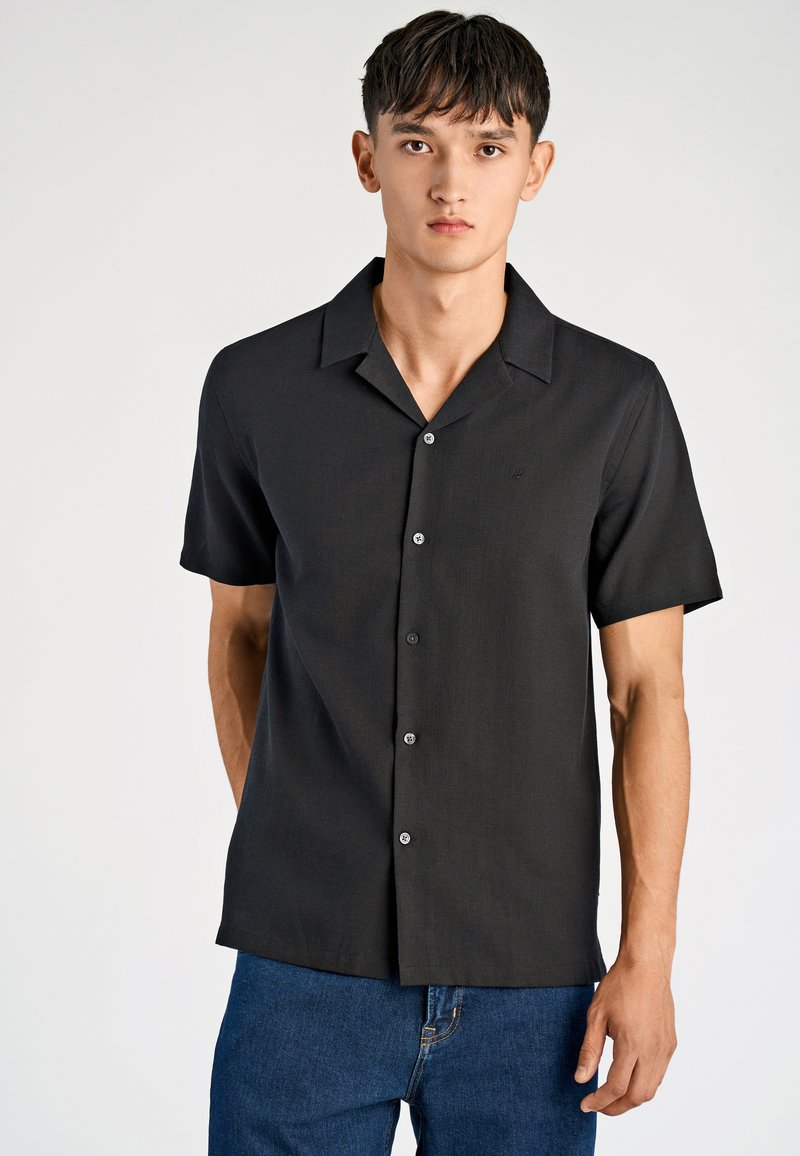 Camicia nera a maniche corte con bottoni in un tessuto leggero, colletto piatto e una sottile texture, caratterizzata da bottoni a contrasto lungo la parte anteriore.