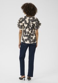 Blusa floreale con maniche a volant, motivo foglie nere su sfondo crema. Abbinata a jeans blu scuro e sandali neri con tacco.