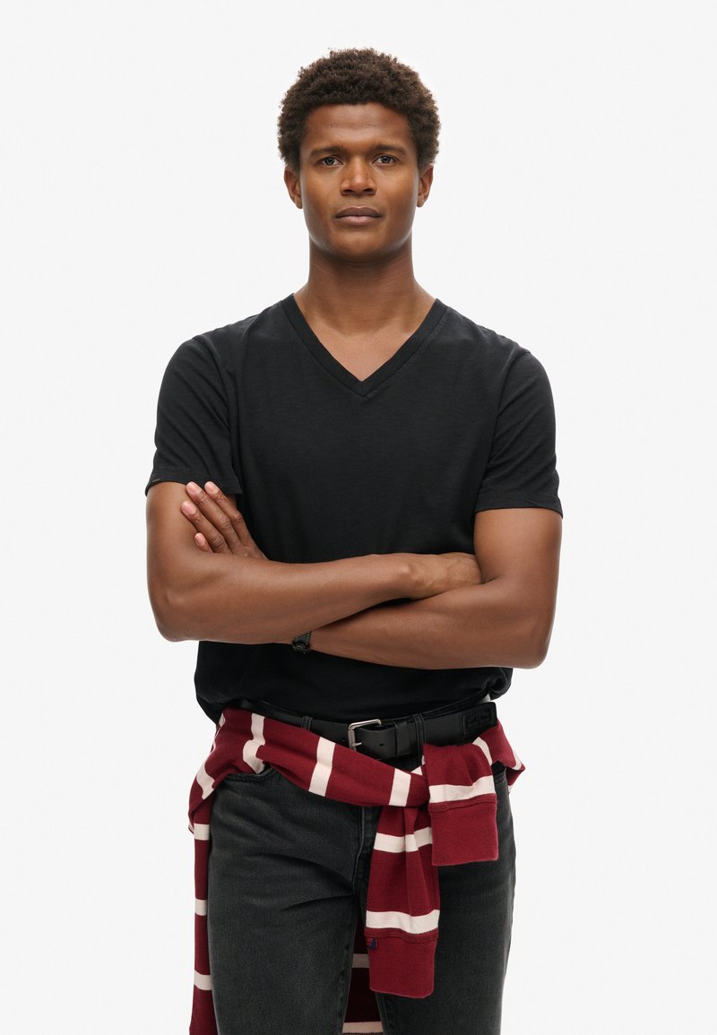 Czarna koszulka z dekoltem w serek i krótkim rękawem, zestawiona z ciemnymi dżinsami. Czerwono-biała sweter w paski jest przewiązany wokół talii.