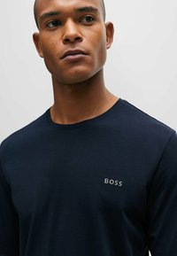 Dunkelblaues Langarm-T-Shirt aus glattem Stoff, mit einem minimalistischen weißen "BOSS"-Logo, das auf der Brustfläche gestickt ist.