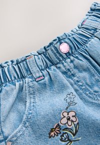 Világoskék farmer rövidnadrág rugalmas derékpánttal, virágos hímzéssel és rózsaszín pattintós gombbal. A dizájn varrási részleteket is tartalmaz.